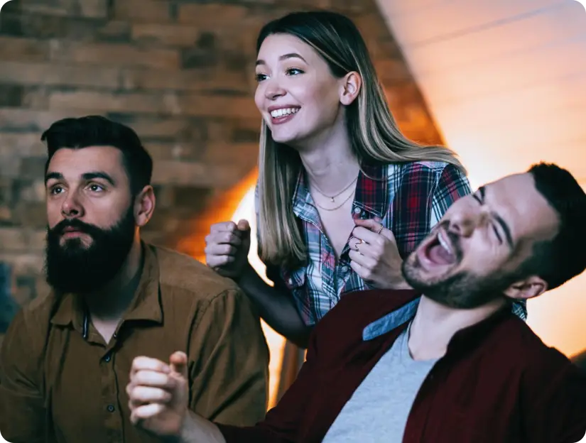 Trois personnes réagissant avec enthousiasme en regardant un écran dans un intérieur.
